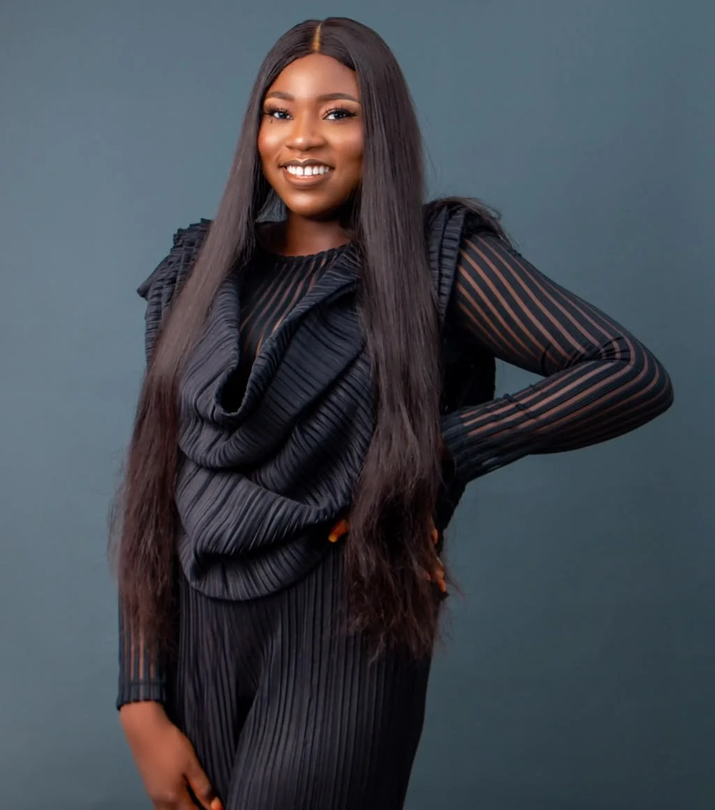 Victory Omoyine Smith Esq in a black pleated outfit against a slate backdrop