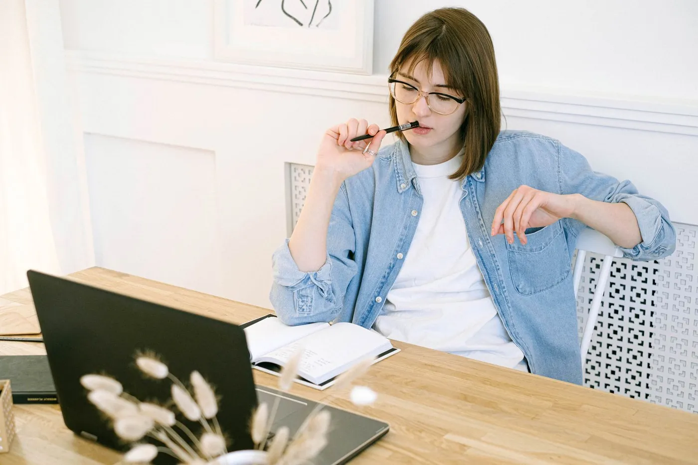 A woman working thoughtfully at a wooden desk with a laptop and notebook
